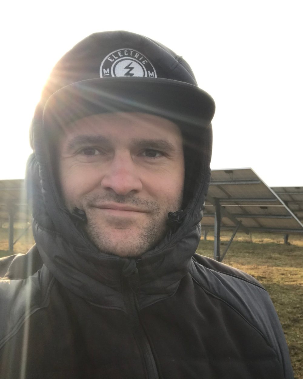 Benjamin Statnik 2016 auf einer Freiflächenanlage, in Winterjacke vor den Modulreihen
